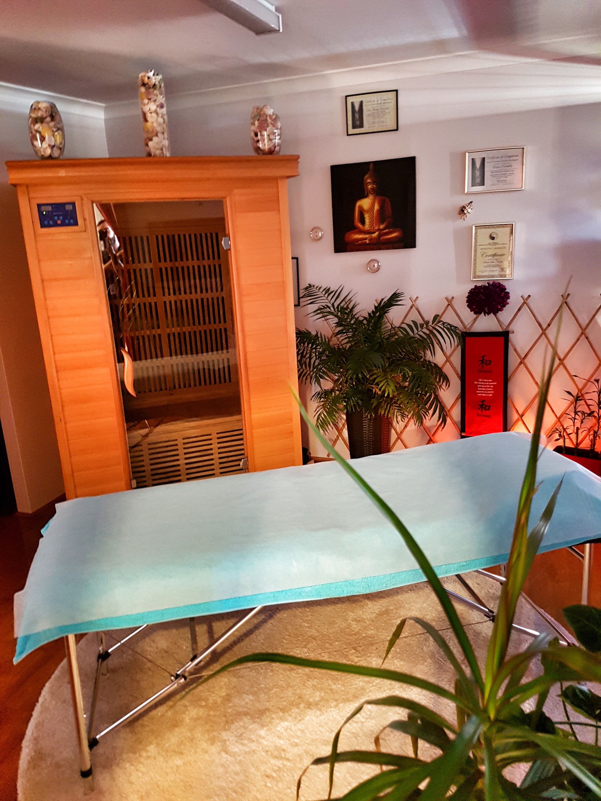 The timber infrared sauna cabin in the corner of the treatment room, next to the made up massage table.