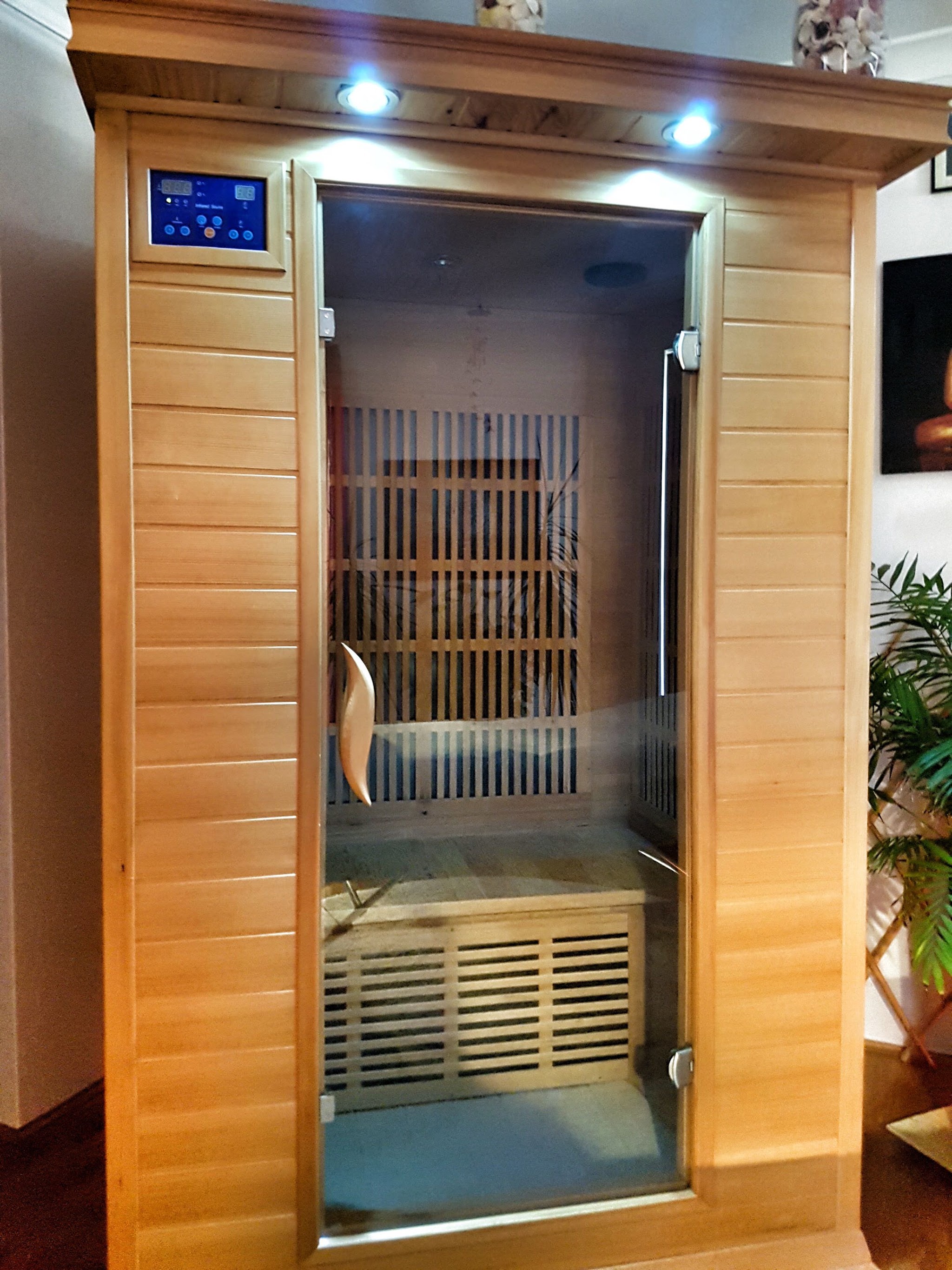 The infrared sauna cabin with its glass door open, showing the timber slat bench inside.