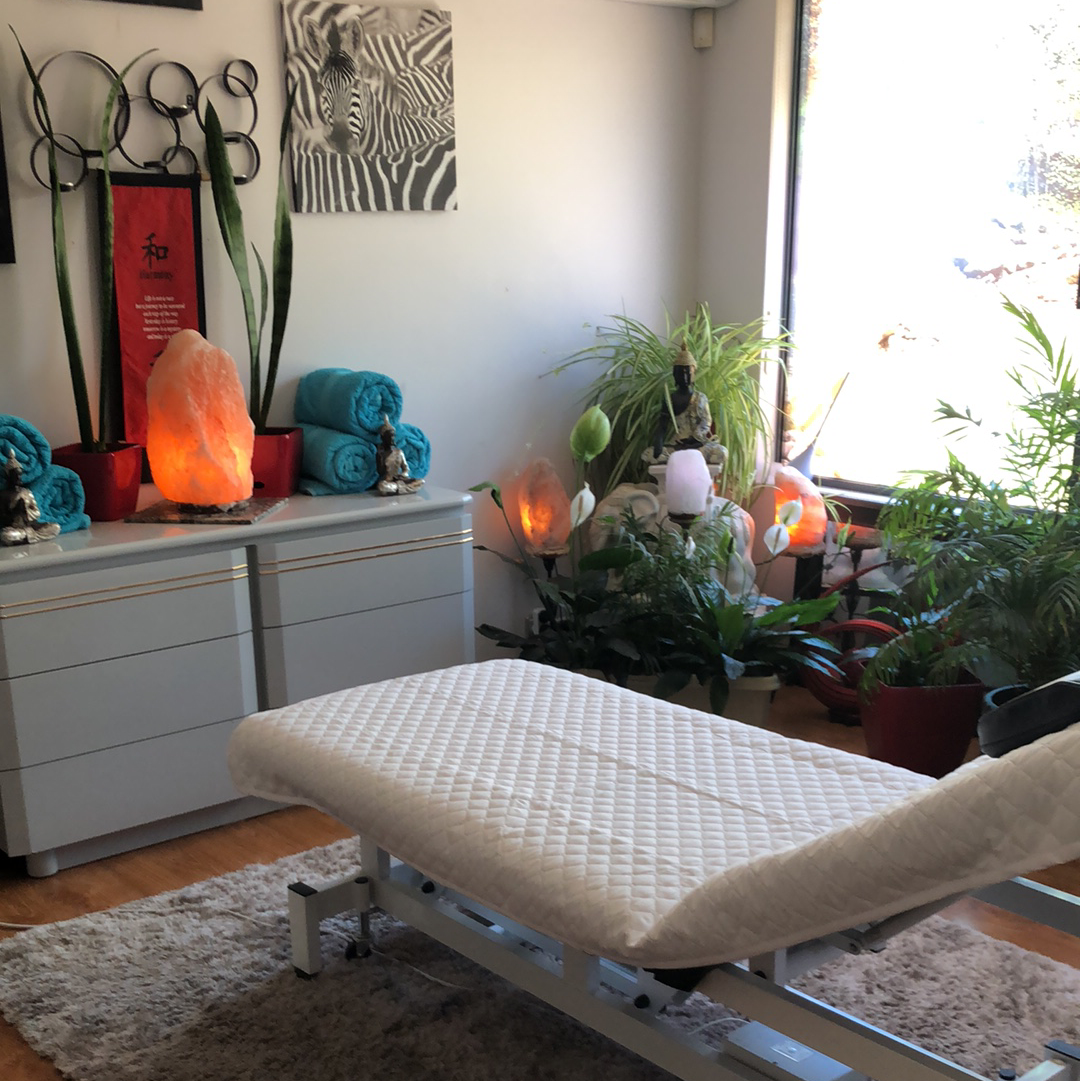 A corner of the studio with rolled teal towels, a salt lamp and small figures on the dresser, lit by the window.